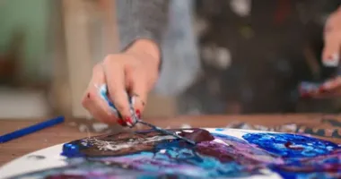 Bir kadın sanatçı yağlı boya ile soyut bir tablo çizer. Bir değnekle akışkan çizim. Beyaz bir tuvalde parlak boya..