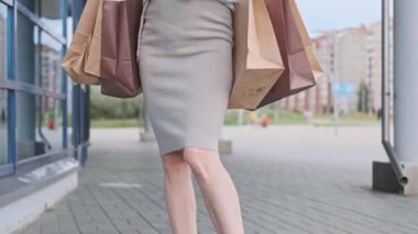 Beyaz kazaklı ve spor ayakkabılı güzel bir sarışın kadın marketten gelen paketlerle caddede yürüyor..