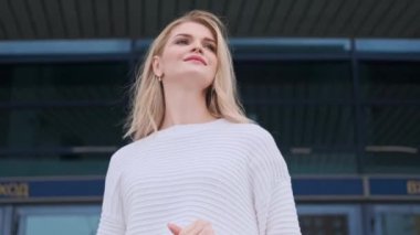 Beyaz kazaklı ve spor ayakkabılı güzel bir sarışın kadın marketten gelen paketlerle caddede yürüyor..