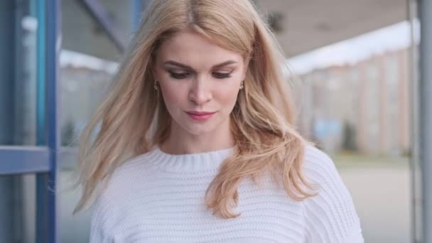 Молода красива блондинка в білому светрі і кросівки йде по вулиці з пакетами з магазину . — стокове відео