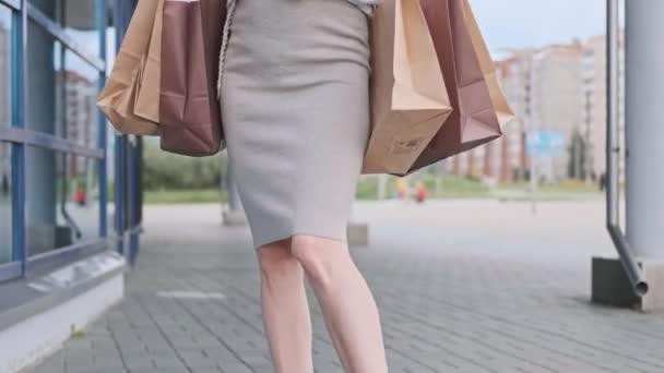 Une jeune belle femme blonde en pull blanc et baskets descend la rue avec des paquets du magasin . — Video