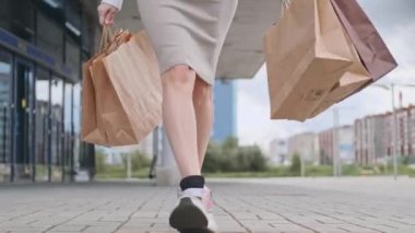 Beyaz kazaklı ve spor ayakkabılı güzel bir sarışın kadın marketten gelen paketlerle caddede yürüyor..