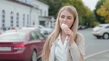 Genç ve çekici sarışın bir kadın sokakta waffle bardağında beyaz bir dondurma boynuzu yiyor..