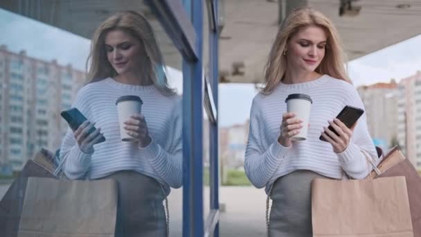 白いセーターとスニーカーを着た若い美しいブロンドの女性が店からのパッケージで通りを歩いています。妊婦の買い物. — ストック動画