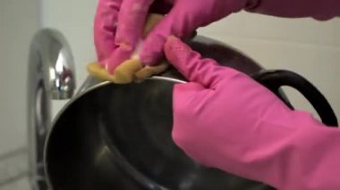 Lastik eldivenli bir kadın, metal bir tencereyi yağlı süngerle yıkıyor..