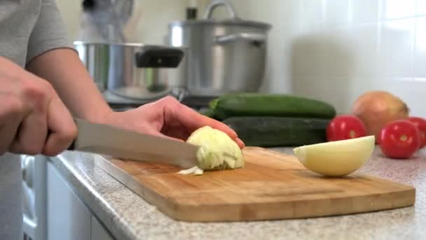 Una donna casalinga cucina a casa in cucina. Affettare la cipolla sul tagliere . — Video Stock