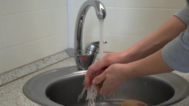 Uma mulher lava batatas e cenouras, limpa legumes para cozinhar sopa . — Vídeo de Stock
