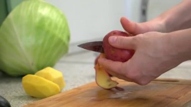 Patates fırçalamak ve doğramak. Rus lahana çorbası pişiriyorum. Bir kadın kesme tahtasıyla sebze kesiyor. Evde yemek pişirmek..