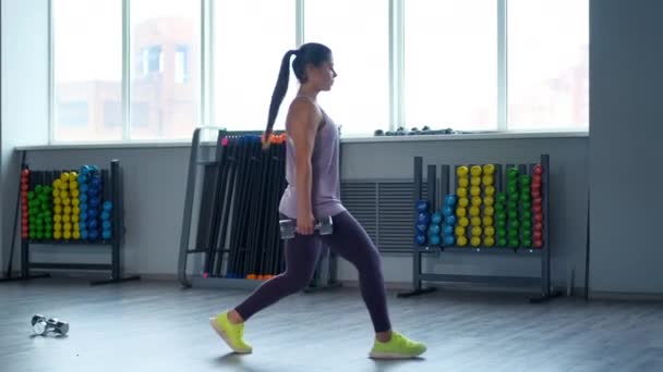 Une belle jeune femme brune sportive dans les trains de vêtements de sport avec des haltères dans la salle de gym . — Video