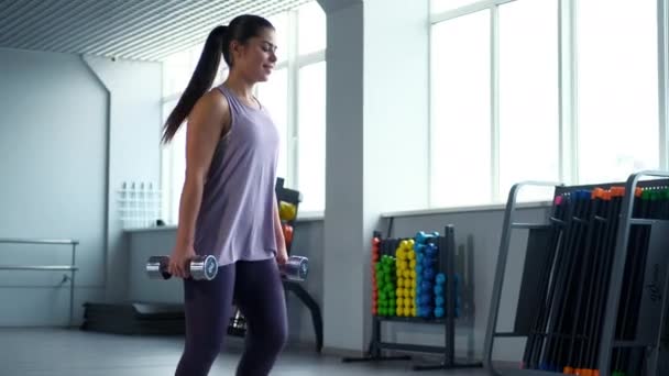 Una hermosa joven morena atlética en trenes de ropa deportiva con mancuernas en el gimnasio . — Vídeo de stock