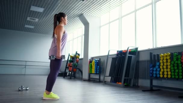 En vacker atletisk ung brunett kvinna i sportkläder tåg med en hantlar i gymmet. — Stockvideo