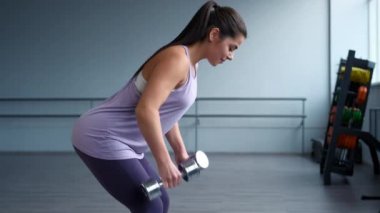 Spor kıyafetleri giymiş, spor salonunda dambılları olan güzel bir esmer kadın..