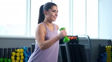 Spor kıyafetleri giymiş, spor salonunda dambılları olan güzel bir esmer kadın..