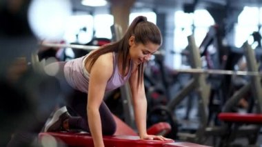 Spor kıyafetleri içinde spor salonunda güzel bir esmer kadın dambılları kaldırıyor..