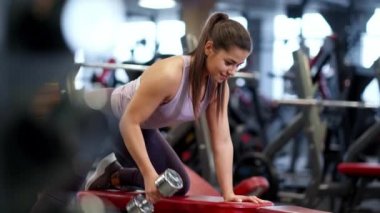 Spor kıyafetleri içinde spor salonunda güzel bir esmer kadın dambılları kaldırıyor..