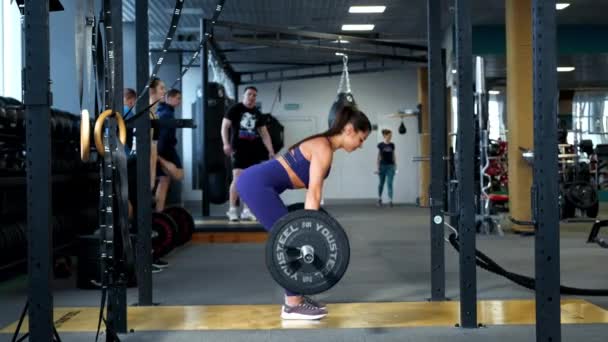 A beautiful athletic young brunette woman in sportswear in the gym performs exercises with a barbell. — Stock Video