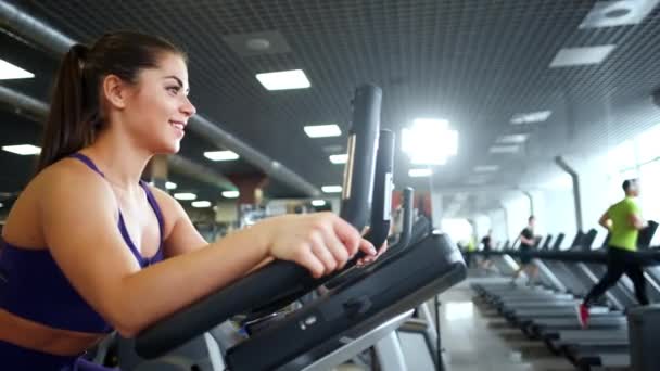En vacker atletisk ung brunett kvinna i sportkläder i gymmet är engagerad på en cykel. — Stockvideo