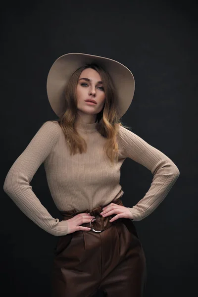 Eine junge sinnliche sexy Frau mit schönem Gesicht und klarer natürlicher Haut posiert im Studio vor schwarzem Hintergrund. Beiger Smoking-Pullover und Hut mit Feldern. — Stockfoto