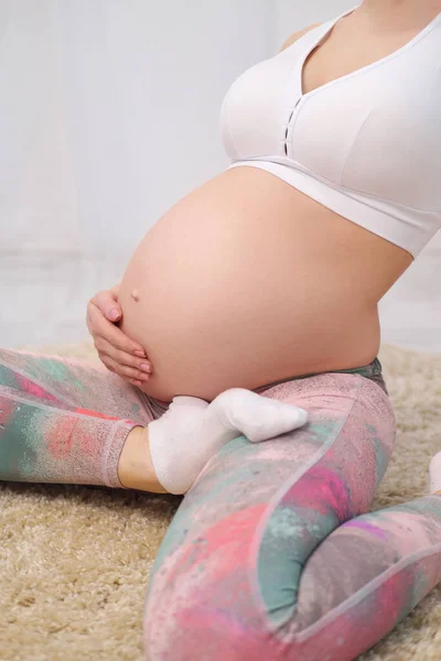 Молода вродлива вагітна кавказька жінка сидить на м "якому килимі будинку. Він займається фітнесом і займається фізичними вправами. Спорткаут. — стокове фото