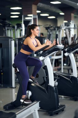 Spor salonunda spor giyim bölümünde güzel bir esmer kadın bisiklete biniyor..