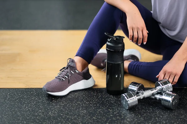 Spor sporu konsepti. Spor aletleri. Bir kadın spor ayakkabılarıyla yerde oturuyor. Bir dambıl ve dambıl.