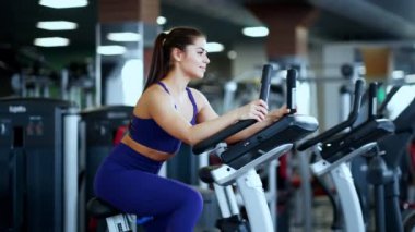 Spor salonunda spor giyim bölümünde güzel bir esmer kadın bisiklete biniyor..