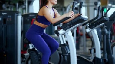 Spor salonunda spor giyim bölümünde güzel bir esmer kadın bisiklete biniyor..
