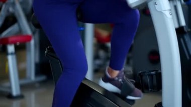 Spor salonunda spor giyim bölümünde güzel bir esmer kadın bisiklete biniyor..