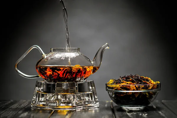 Horizontal photo of the tea set on a black background. Glass transparent teapot and cup. Black leaf tea.