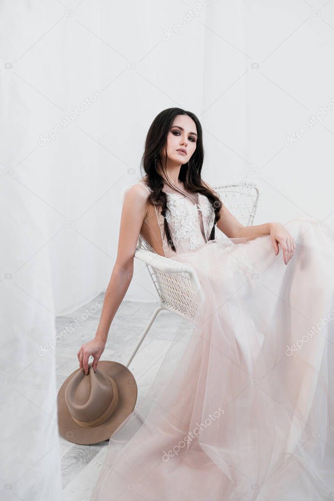 Portrait of bride. A young attractive brunette woman with long black hair in braids. White wedding dress and beige hat. Rustic style, bouquet of wheat spikes.