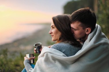 Birbirine aşık bir çift gün batımında nehir kenarında oturur. Sarılırlar, ekoseye sarınırlar ve metal bir bardaktan çay içerler..