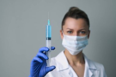 Beyaz cüppeli ve maskeli bir kadın doktor elinde bir şırınga tutuyor..
