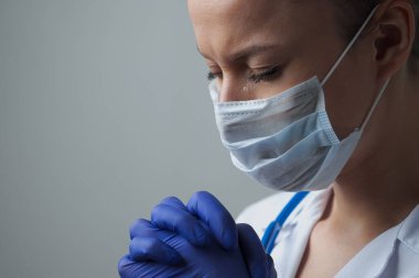 Beyaz cüppeli, maskeli ve eldivenli bir kadın doktor. Yüzü yakın plan. Doktor ağlar ve dua eder. Gözyaşları. Salgın ve virüs salgını. Coronavirus covid-19.