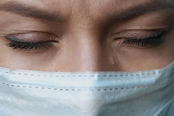 Eine Ärztin in weißem Gewand, Maske und Handschuhen. Gesicht aus nächster Nähe. Der Arzt weint und betet. Tränen in den Augen. Pandemie und Virusepidemie. Coronavirus covid-19. — Stockfoto