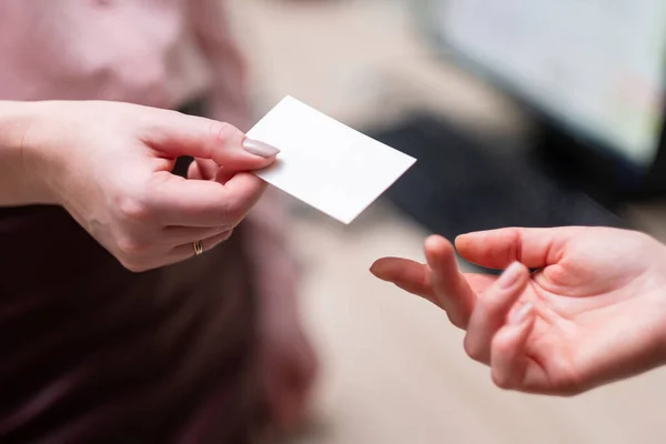 Una mujer le da a otra una tarjeta de visita. Un primer plano de dos manos . — Foto de Stock