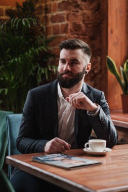 Pencerenin karşısındaki restoranda yakışıklı, şık, sakallı bir adam, Kavkuzets Chdmt. Dergi okuyor, kahve içiyor..