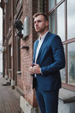 Takım elbiseli, sakallı, genç ve yakışıklı bir adam şehrin caddesinde duruyor..