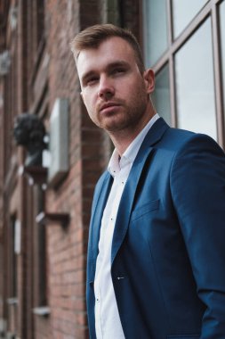 Takım elbiseli, sakallı, genç ve yakışıklı bir adam şehrin caddesinde duruyor..