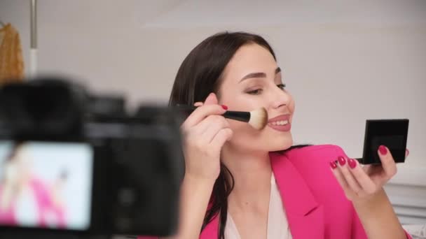 Uma bela jovem blogueira em uma jaqueta rosa atira em um blog sobre cosméticos. Fica em casa. Auto-isolamento e quarentena . — Vídeo de Stock
