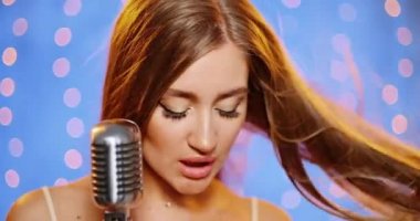 Uzun saçlı, pullu bir gece elbisesi içinde güzel, genç ve seksi bir kadın. Klasik bir mikrofonda şarkı söyleyen, dans eden ve gülümseyen bir kız..