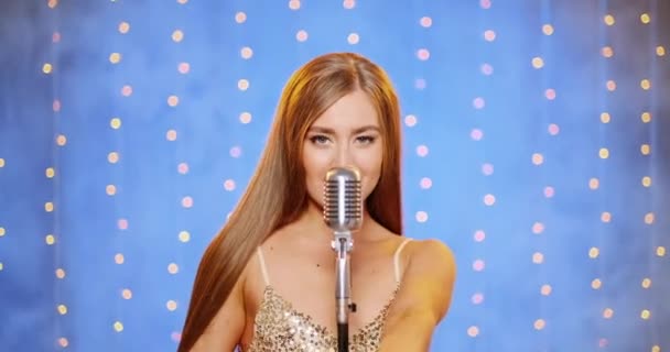 Een mooie jonge sexy vrouw met lang haar in een avondjurk met pailletten. Meisje zingt op het podium in een vintage microfoon, danst en glimlacht. — Stockvideo