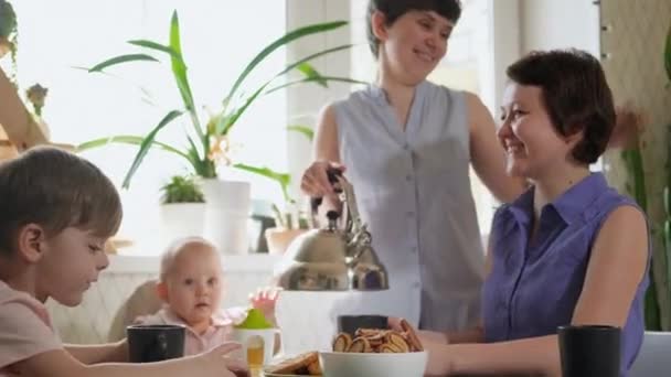 Una familia lesbiana homosexual con dos hijos y madres se sienta en la cocina en una mesa y desayuna. Estilo de vida . — Vídeos de Stock