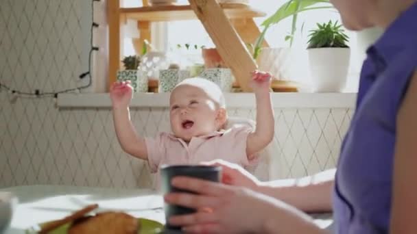 Ein kleines Mädchen sitzt auf einem Kinderstuhl an einem Tisch in der Küche und lächelt. — Stockvideo