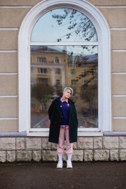 Kısa saç kesimi ve boyalı saçı olan yeşil ceketli güzel bir kadının portresi. Gri ana renk ve sarı, yeşil, mavi ve kırmızı saç rengi.