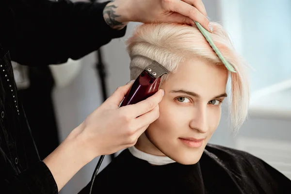 Máquina de cabeleireiro corta cliente mulher. Um corte de cabelo curto, templo raspado e um desenho no cabelo . — Fotografia de Stock