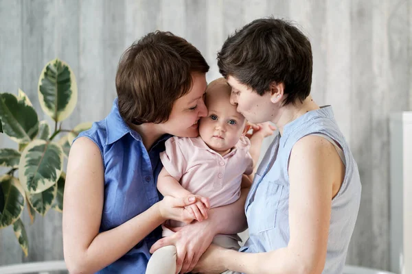 Una giovane coppia lesbica gay con un bambino tra le braccia. Stanno posando a casa. . — Foto Stock
