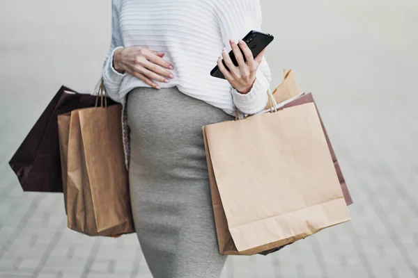 Pregnant shopper woman with bags from the store. Belly and legs close-up. White sweater, skirt and sneakers.