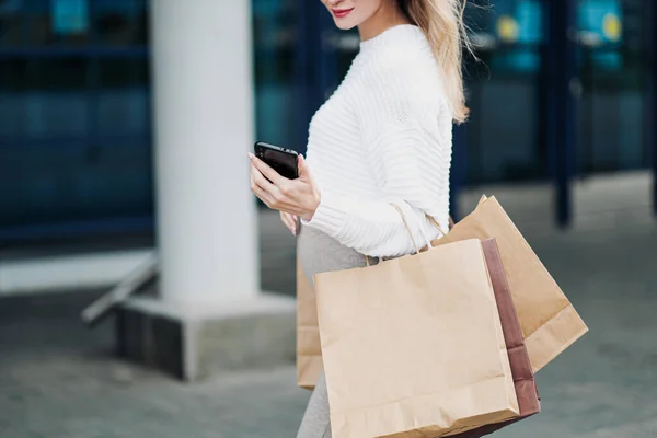 Mujer compradora embarazada con bolsas de la tienda. Vientre y piernas de cerca. Jersey blanco, falda y zapatillas deportivas . —  Fotos de Stock
