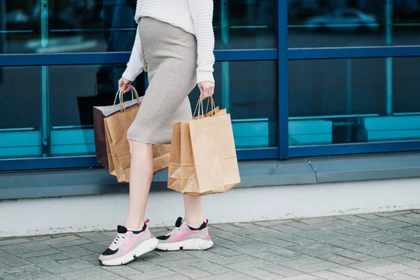 Gravid shopper kvinde med poser fra butikken. Maven og benene er tæt på. Hvid sweater, nederdel og sneakers . - Stock-foto