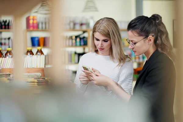 Een jonge aantrekkelijke blonde vrouw in een witte trui shopper in de winkel kiest crème. Cosmetica en schoonheidssalon. — Stockfoto